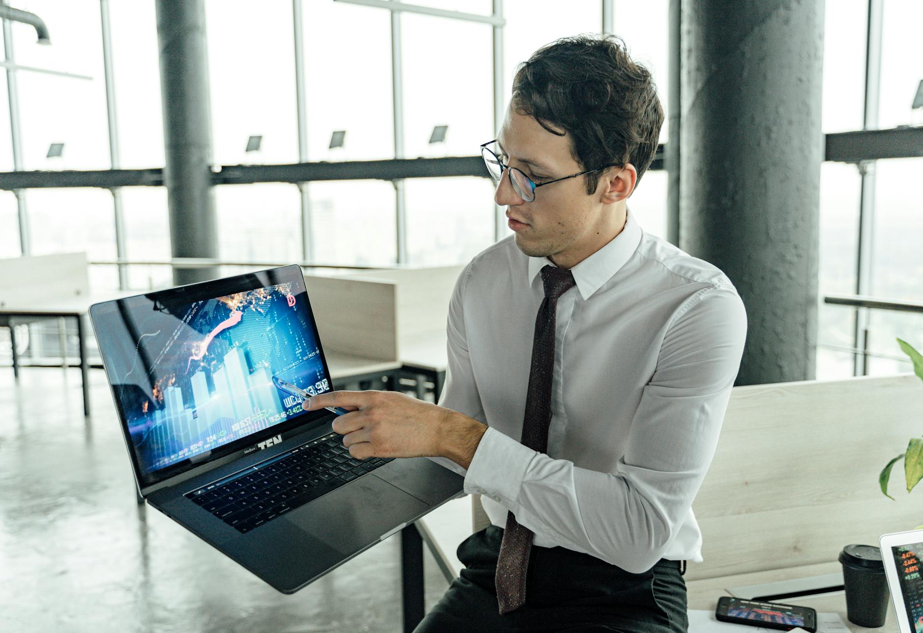 A businessman in an office analyzing market trends on a laptop with graphs and charts displayed.