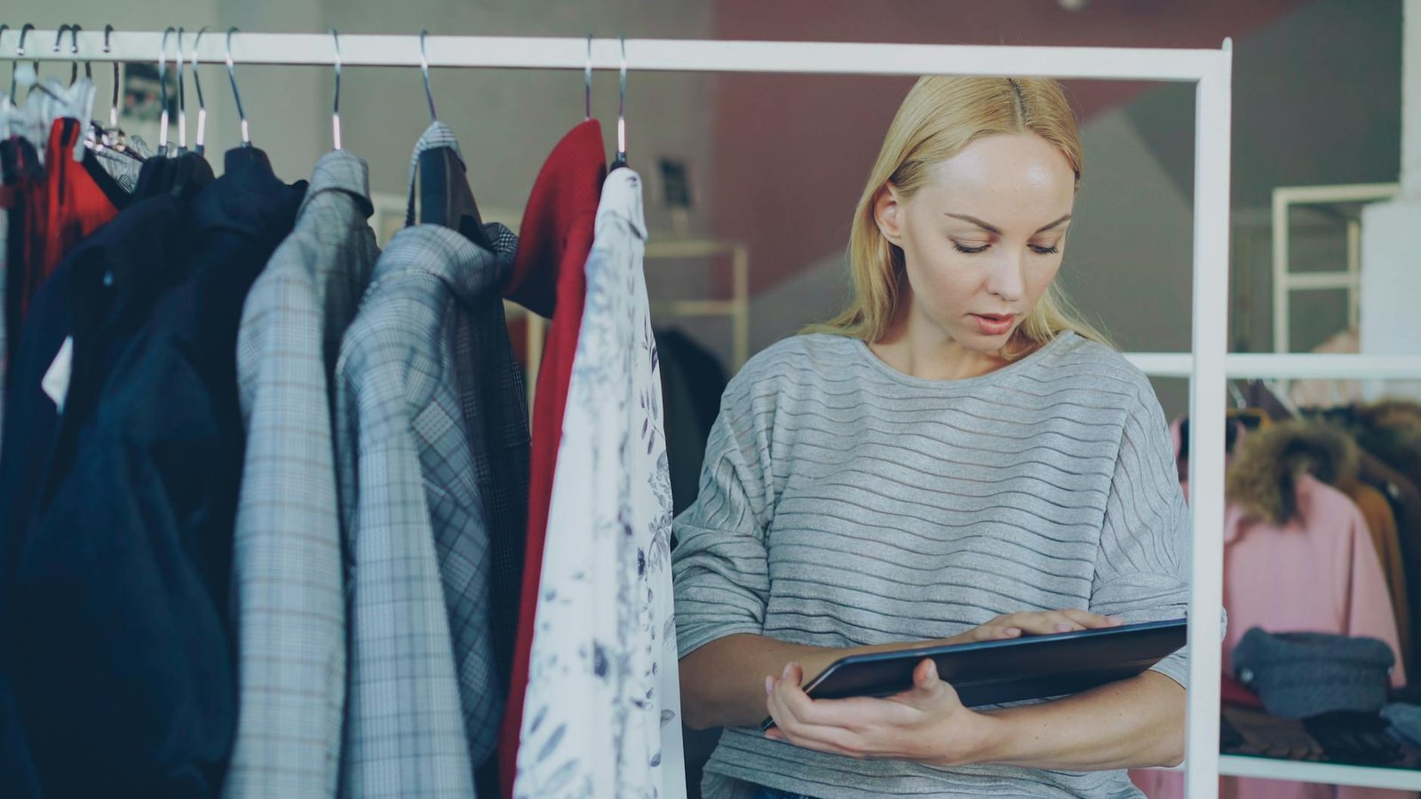 Woman employee checking inventory using a tablet in a clothing store.