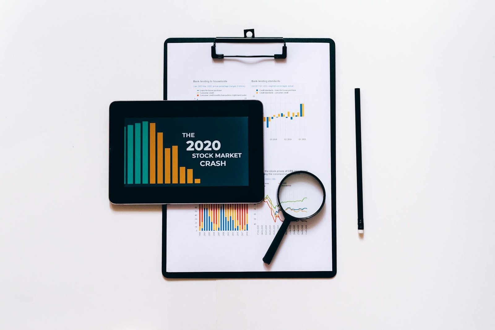 Tablet, magnifying glass, and clipboard for stock market analysis.