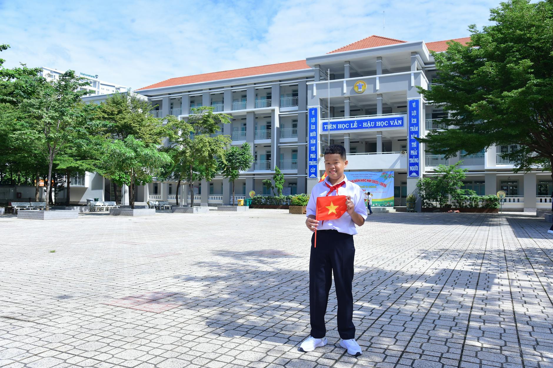 Young Vietnamese student holding national flag in bright schoolyard setting.
