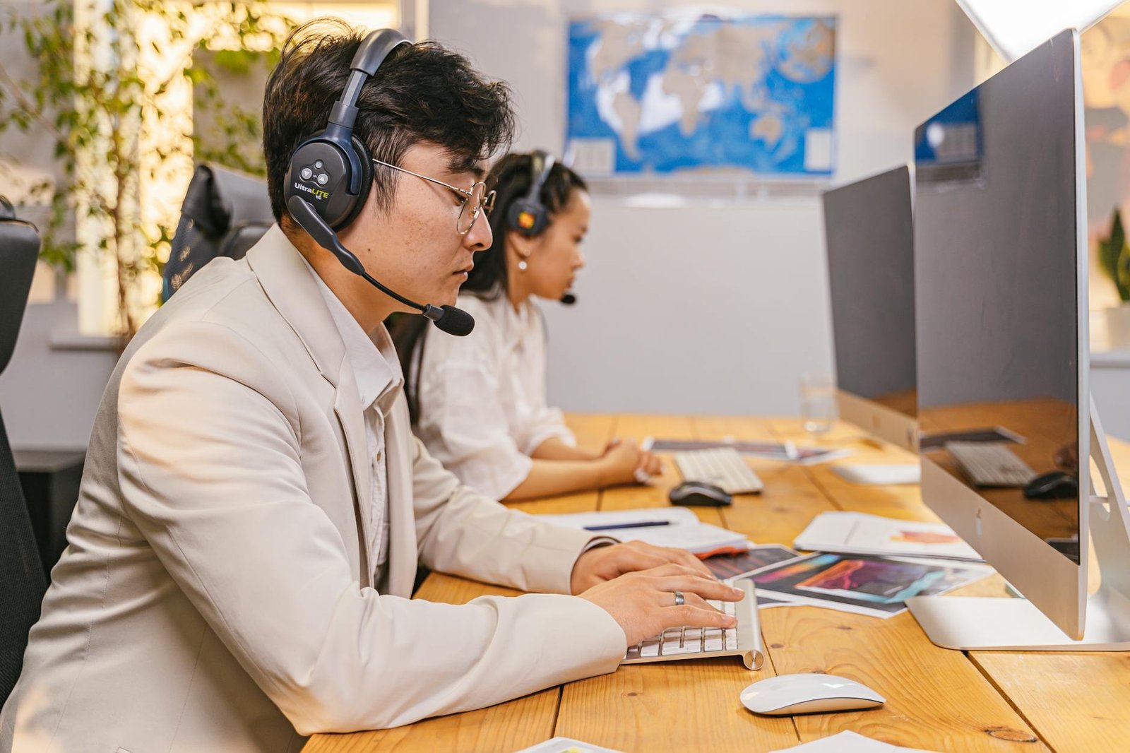 Two colleagues at desks wearing headsets and working on computers in a modern office.