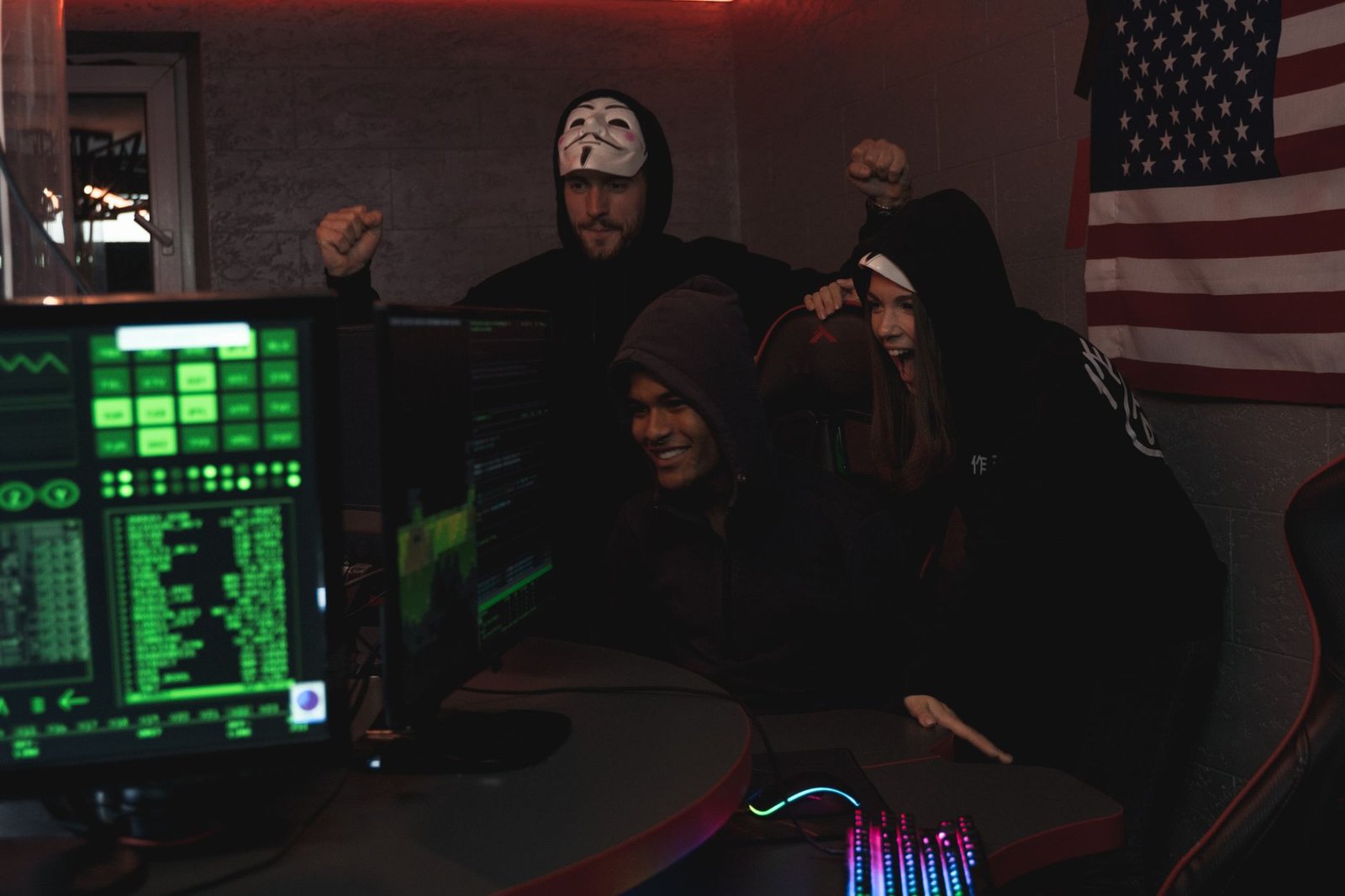 Group of tech enthusiasts in hoodies celebrate a successful cybersecurity operation indoors.