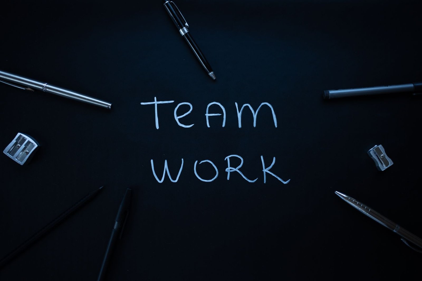 Arrangement of office supplies around teamwork text on black background.